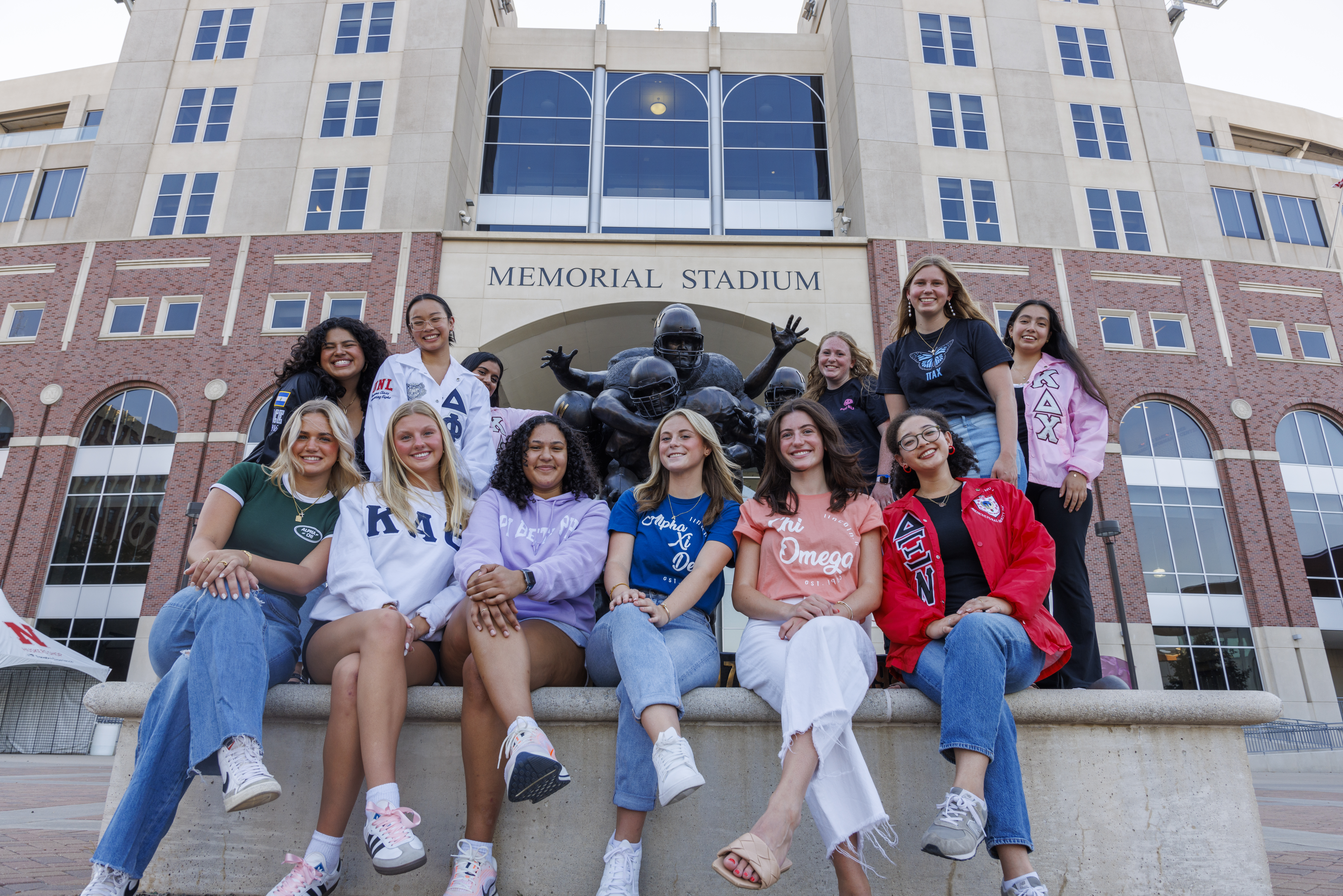 Group of people smiling in front of Memorial Stadium statue, wearing colorful clothing.