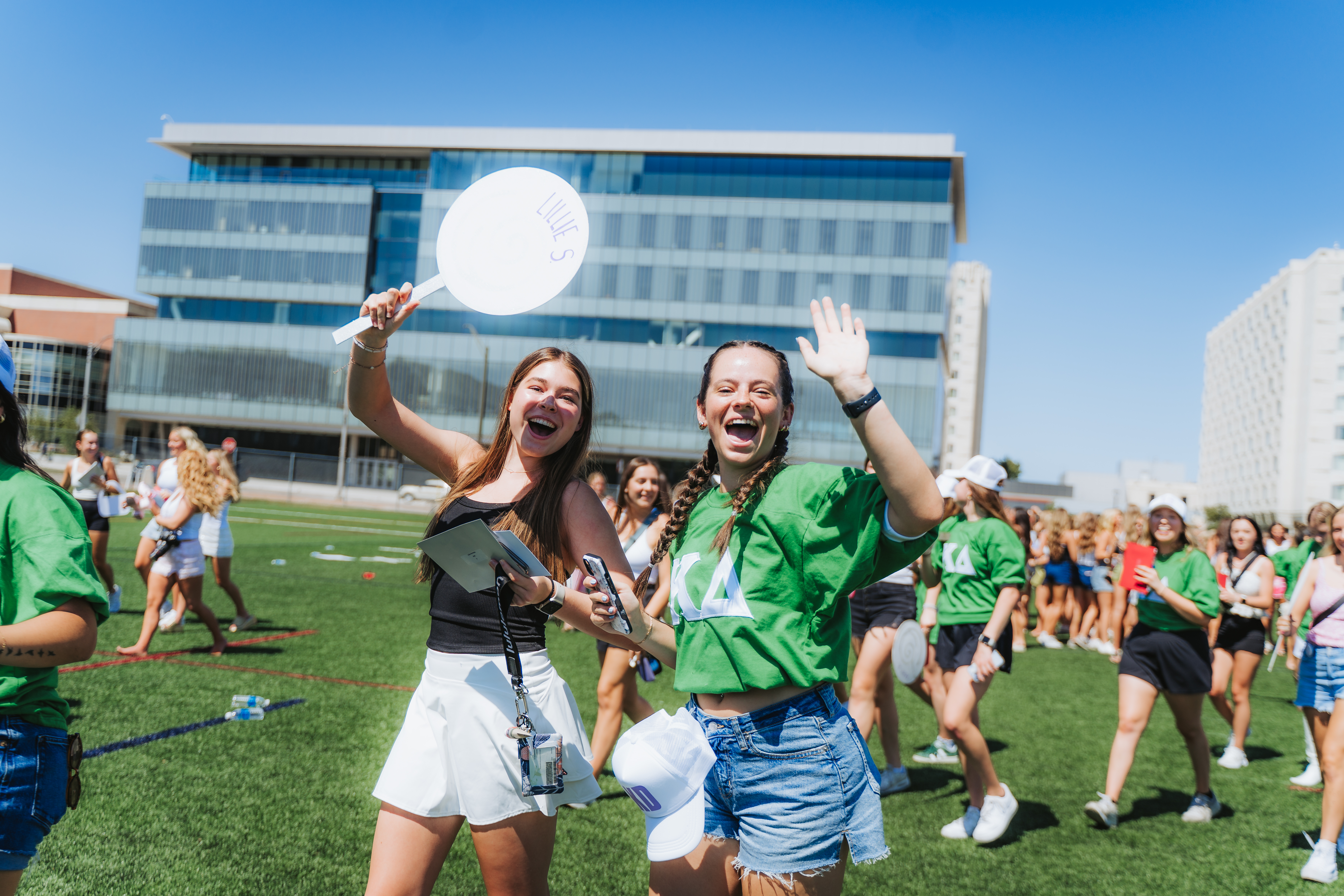 People celebrating outdoors on a sunny day, wearing green shirts near large modern buildings.