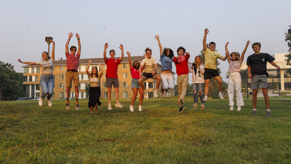 Fraternity and sorority members jump in the air in the green space.