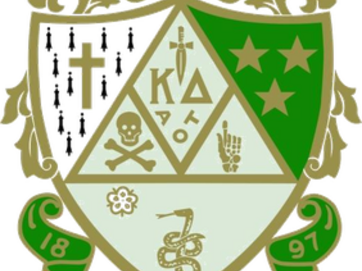 Fraternity crest with symbols including stars, a skull, a snake, a cross, and green and gold accents.